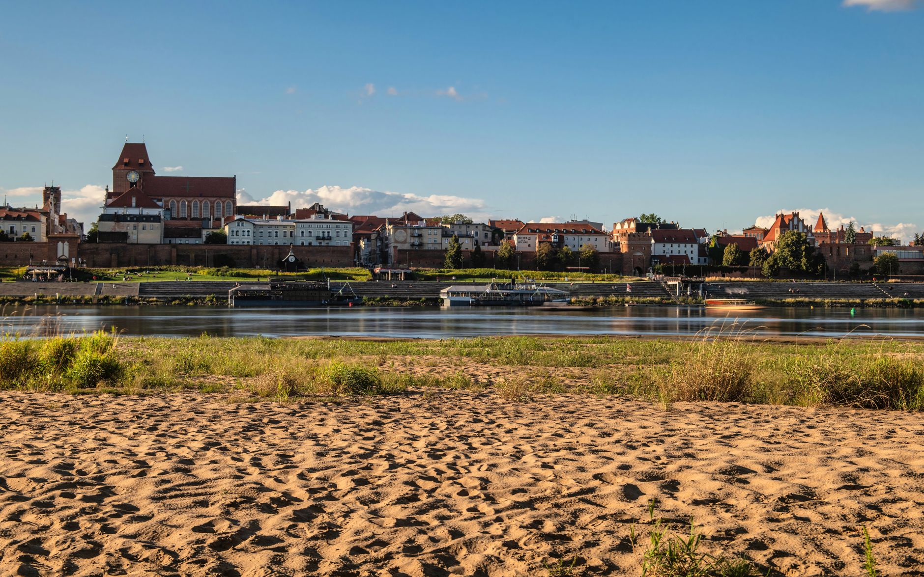 Panoramic view of Toruń's historic riverfront on a sunny day, showcasing its iconic architecture.