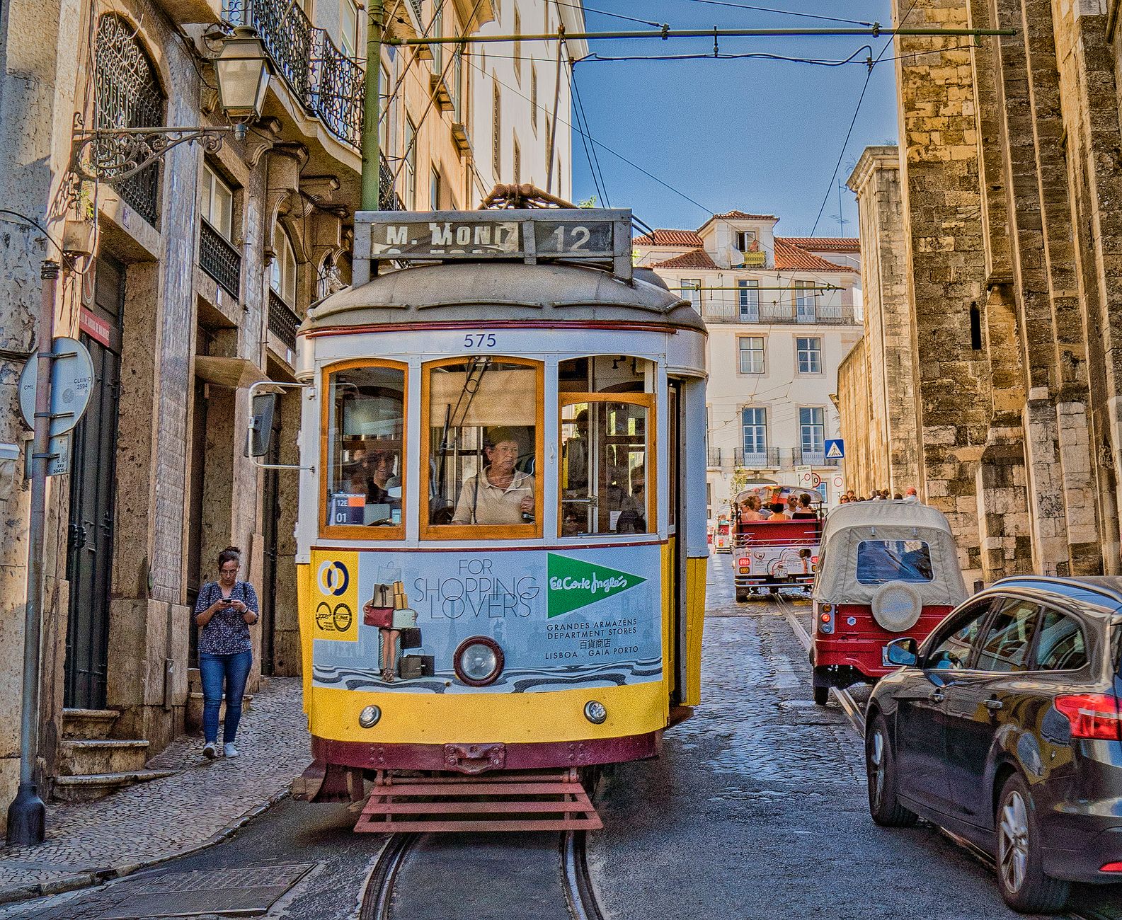 Vintage yellow tram navigating narrow streets of historic Lisbon, capturing city life.