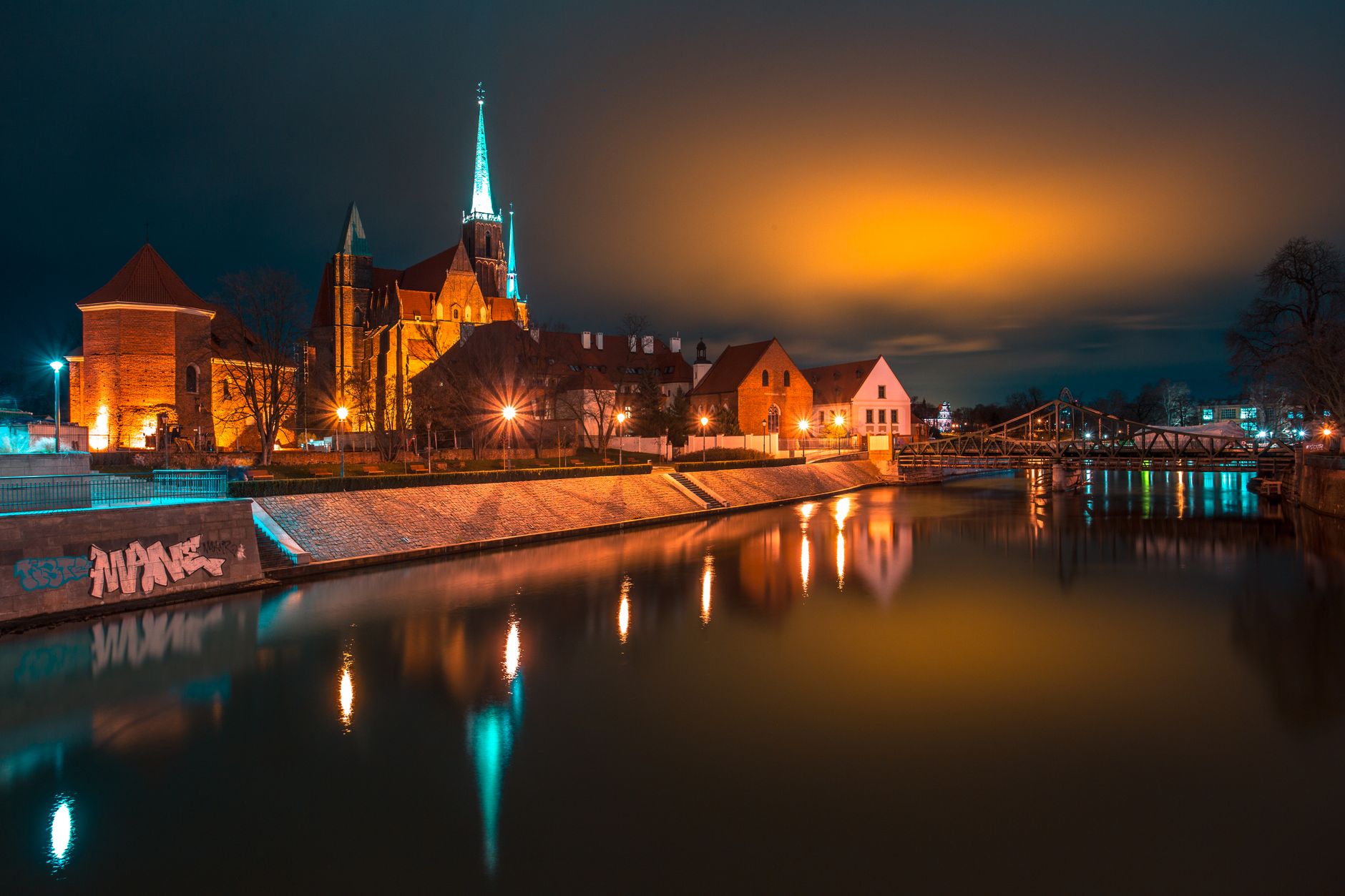 Stunning nighttime view of Wrocław Cathedral and Odra River reflecting the city lights.