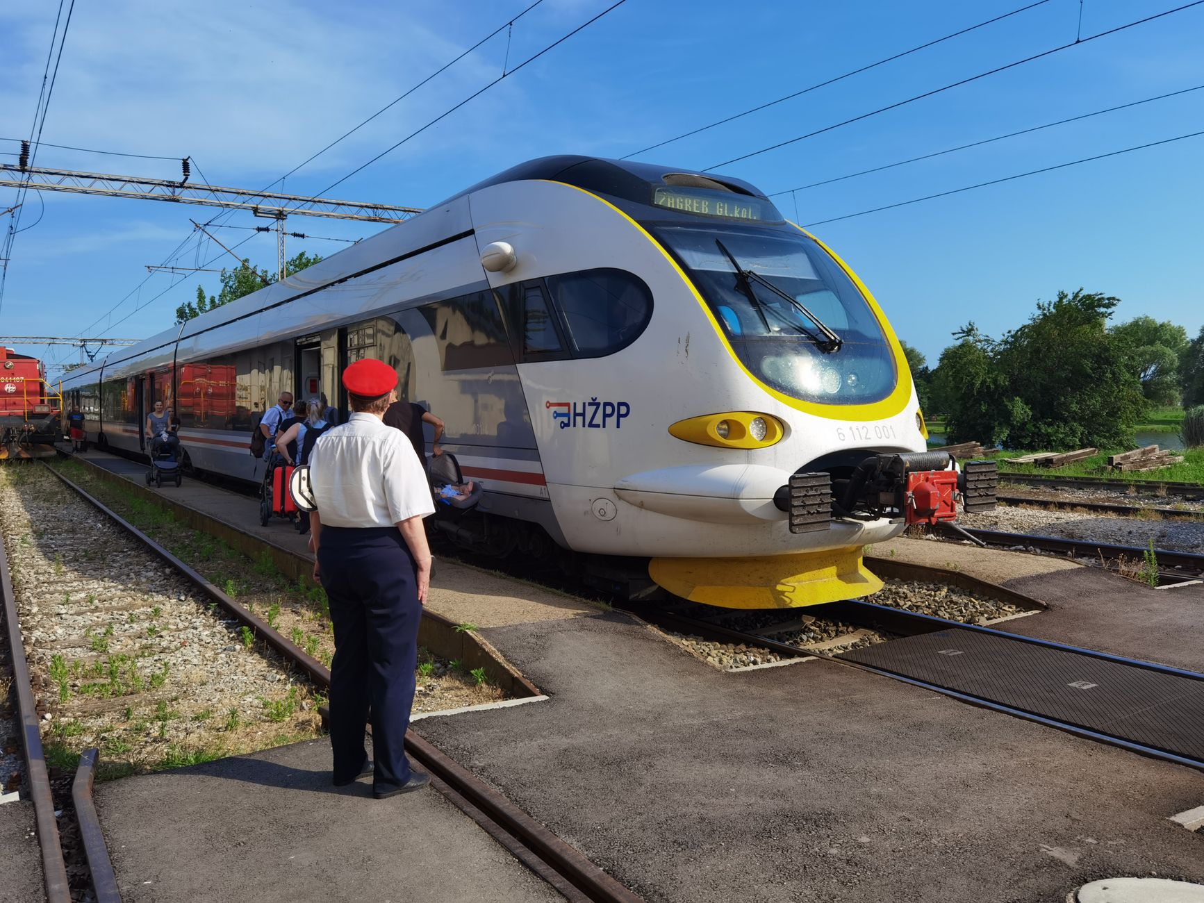 A modern train at a railway station with commuters boarding and a conductor overseeing.