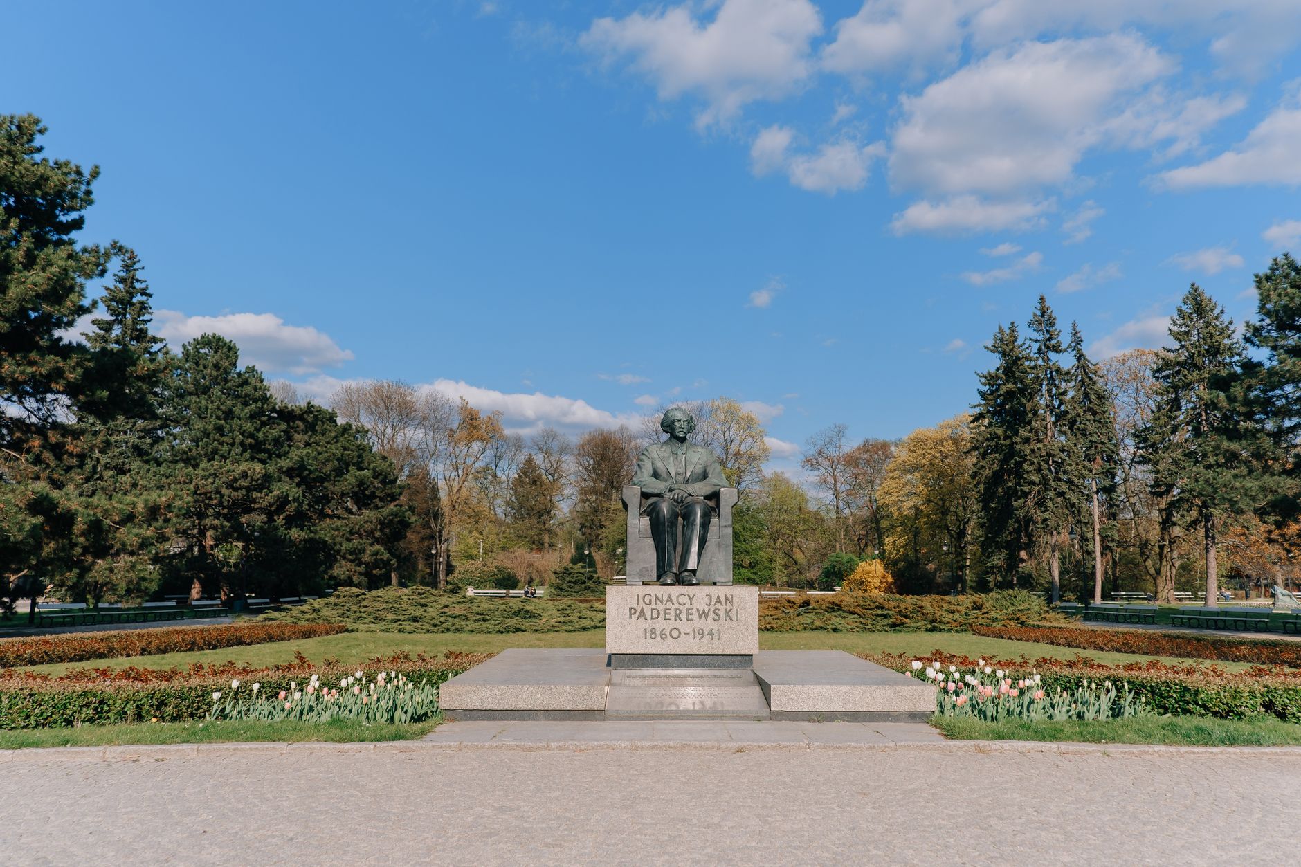 Statue of Ignacy Jan Paderewski in blooming Ujazdowski Park, Warsaw under clear blue sky.