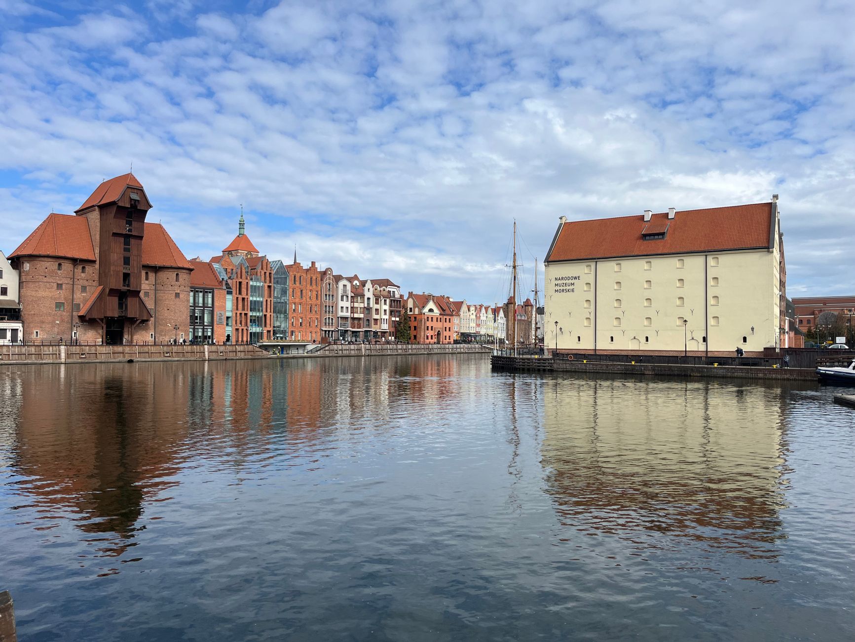 Beautiful Gdańsk waterfront with historical buildings and reflections under blue skies.